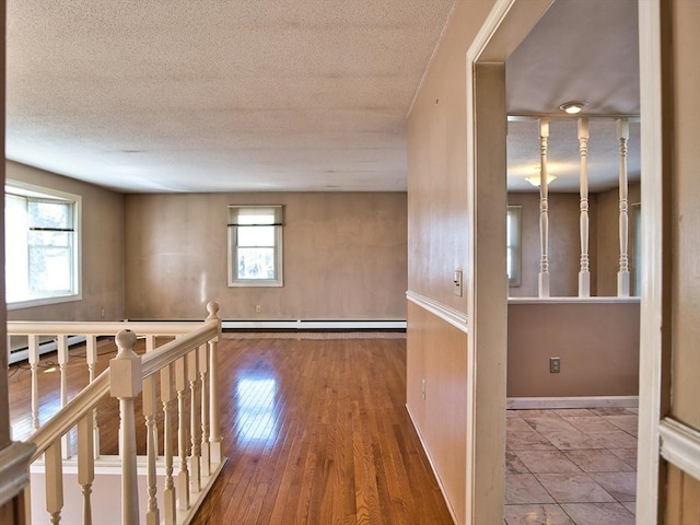 hall featuring an upstairs landing, a textured ceiling, baseboards, and wood-type flooring