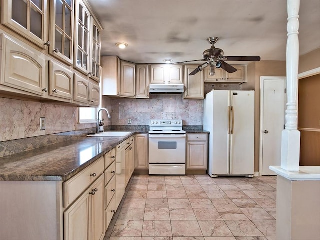 kitchen with dark countertops, under cabinet range hood, decorative backsplash, white appliances, and a sink