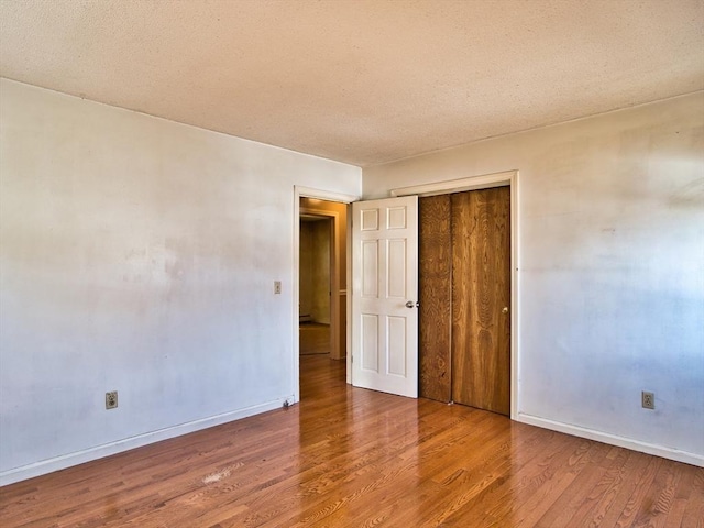 unfurnished bedroom featuring a closet, a textured ceiling, baseboards, and wood finished floors