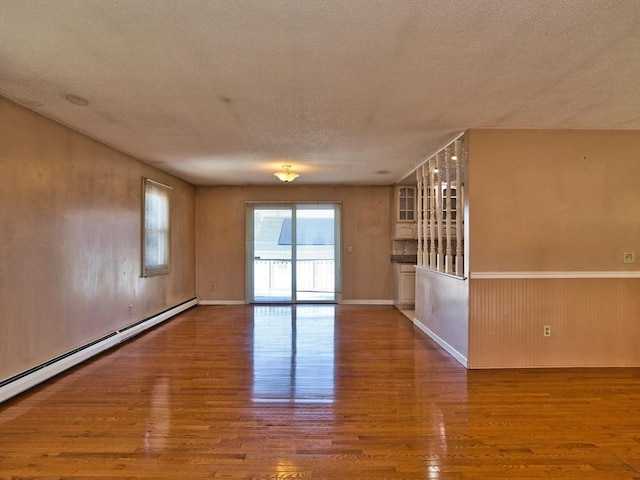 spare room featuring wood finished floors, a wainscoted wall, baseboard heating, and a textured ceiling