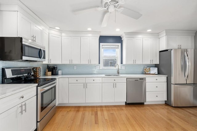 kitchen with light wood finished floors, light countertops, appliances with stainless steel finishes, white cabinetry, and a sink