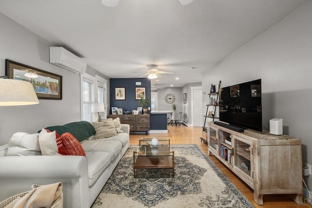 living area featuring a wall unit AC, light wood-type flooring, and ceiling fan