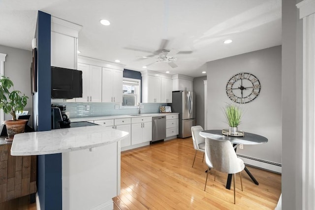 kitchen with baseboard heating, light wood-style flooring, a peninsula, stainless steel appliances, and a sink