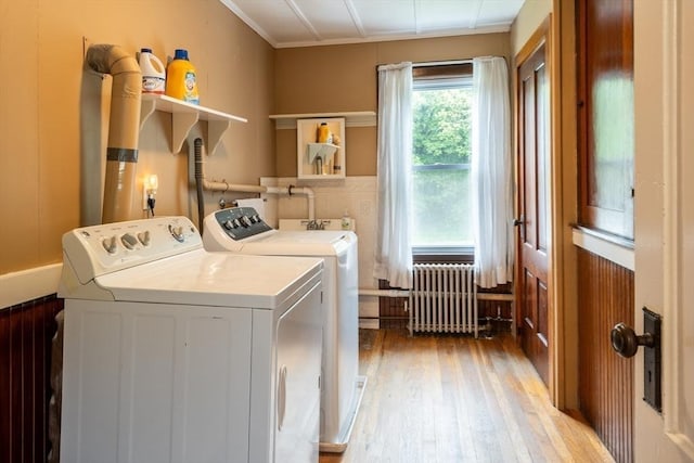 clothes washing area featuring radiator, washer and clothes dryer, and light wood-style flooring