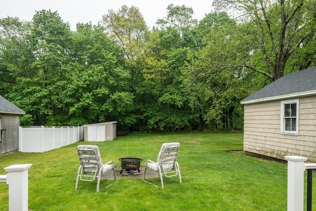 view of yard featuring an outdoor fire pit, a storage unit, an outdoor structure, and view of wooded area