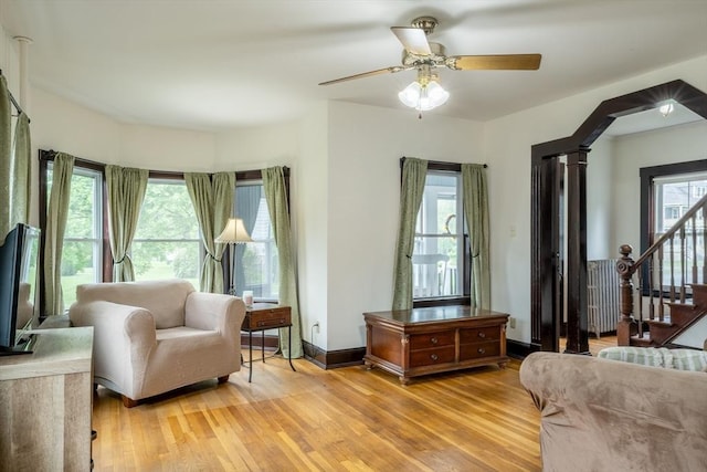 sitting room featuring light wood-type flooring, stairway, a ceiling fan, and decorative columns