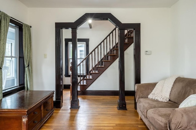 living area with healthy amount of natural light, wood finished floors, decorative columns, and stairs