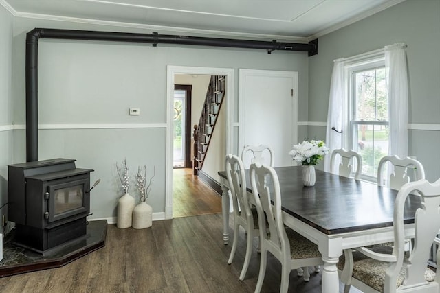 dining room featuring dark wood finished floors, a wood stove, stairway, and crown molding