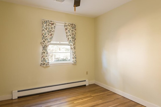 spare room featuring a baseboard radiator, ceiling fan, baseboards, and wood finished floors