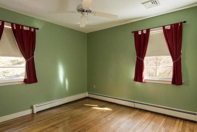 spare room with visible vents, ceiling fan, baseboard heating, and wood finished floors