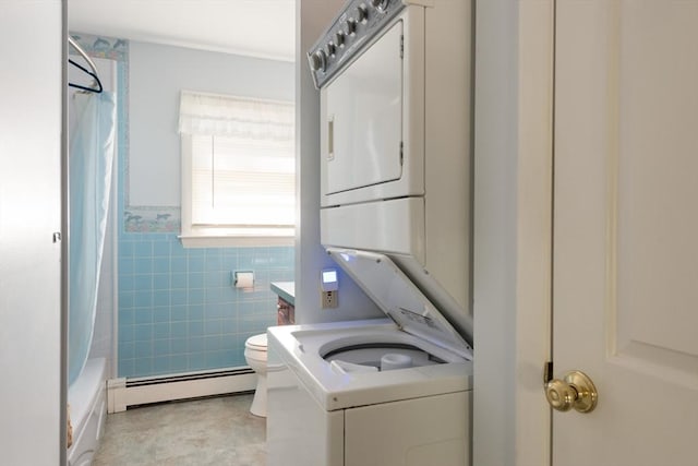 washroom featuring a baseboard heating unit, stacked washer and dryer, a wainscoted wall, laundry area, and tile walls