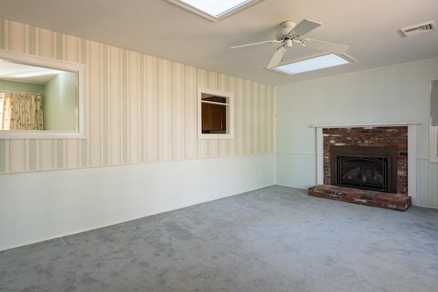 unfurnished living room with ceiling fan, a fireplace, visible vents, carpet, and wallpapered walls