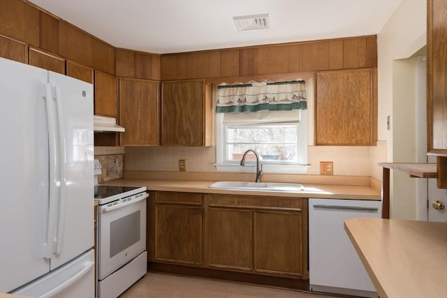 kitchen featuring under cabinet range hood, white appliances, a sink, visible vents, and light countertops