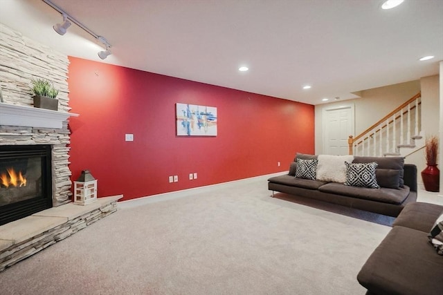 carpeted living room with rail lighting and a stone fireplace