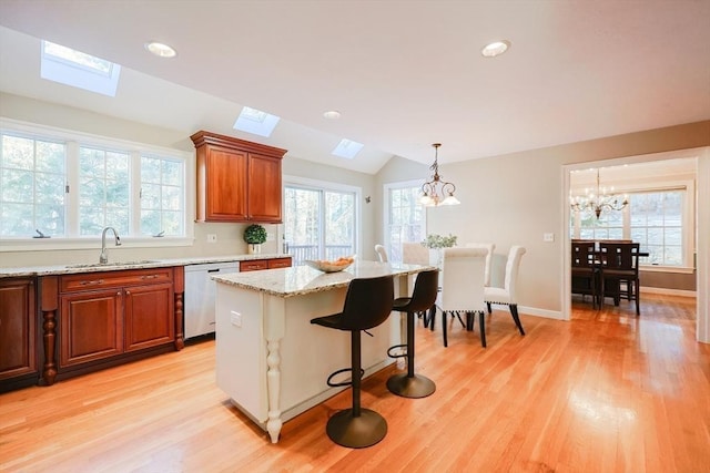 kitchen with a kitchen island, vaulted ceiling with skylight, sink, a kitchen breakfast bar, and stainless steel dishwasher