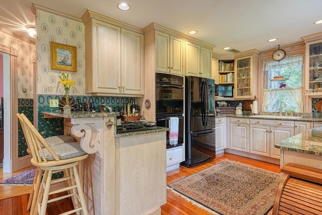 70 Main St, Northborough, MA 01532 - kitchen featuring black appliances, a sink, a breakfast bar area, glass insert cabinets, and light stone countertops
