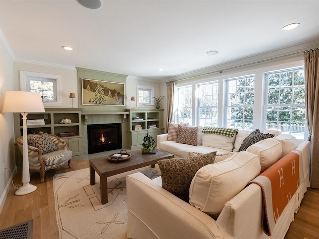 living room featuring a large fireplace, a wealth of natural light, ornamental molding, and light hardwood / wood-style flooring