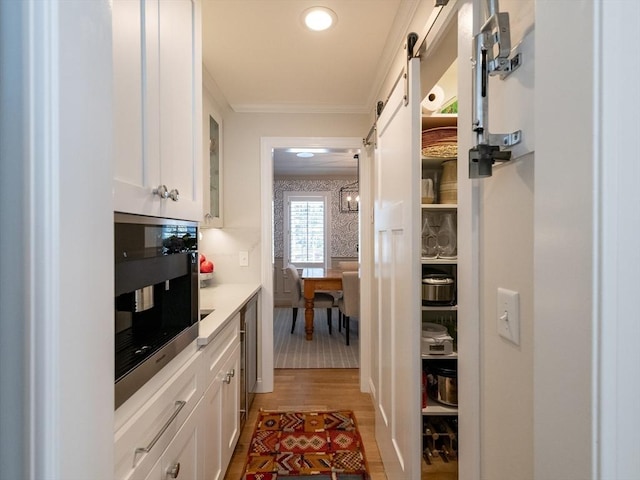 kitchen with white cabinetry, a barn door, light wood-type flooring, hanging light fixtures, and crown molding