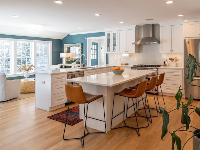 kitchen featuring kitchen peninsula, appliances with stainless steel finishes, wall chimney exhaust hood, and a kitchen bar