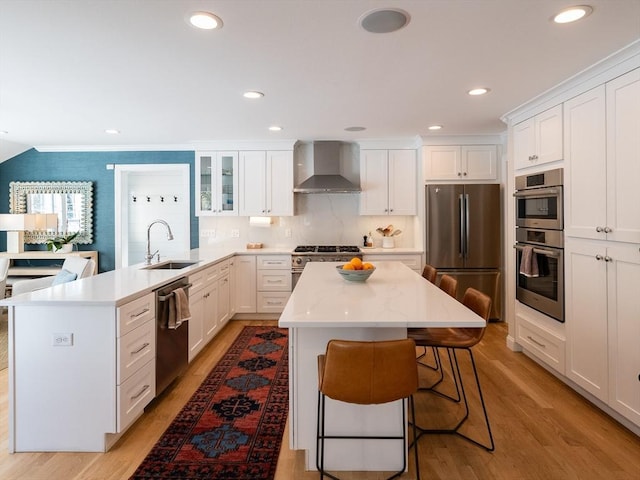 kitchen with sink, white cabinetry, a breakfast bar area, stainless steel appliances, and wall chimney exhaust hood