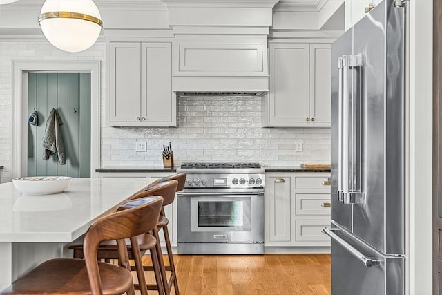 kitchen with tasteful backsplash, a kitchen bar, high end appliances, light hardwood / wood-style floors, and crown molding