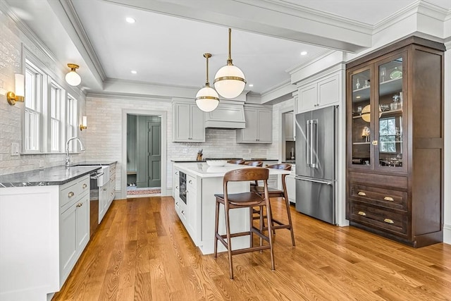 kitchen with high end refrigerator, a center island, hanging light fixtures, and light hardwood / wood-style flooring