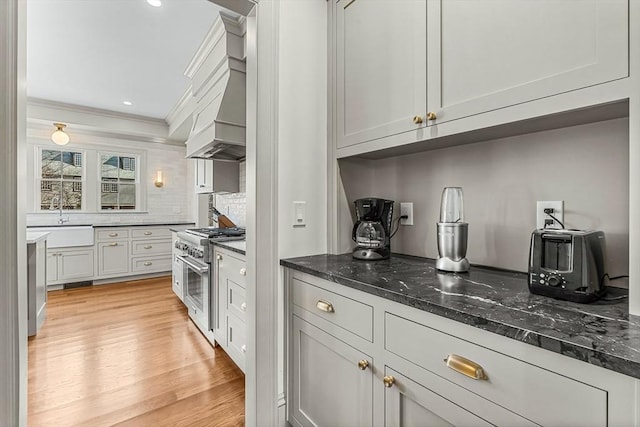 kitchen featuring high end stainless steel range oven, sink, dark stone countertops, and light hardwood / wood-style floors