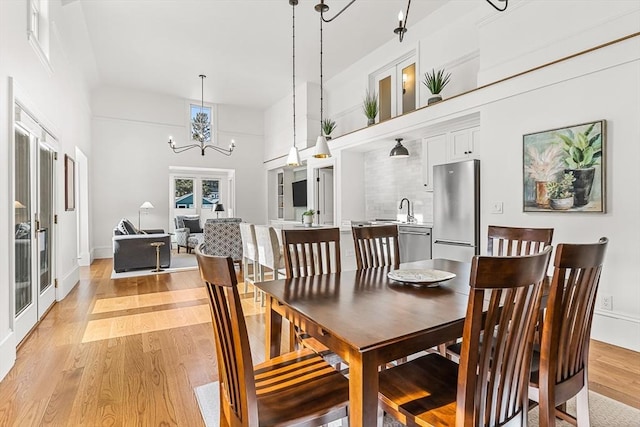 dining space featuring a towering ceiling, an inviting chandelier, light hardwood / wood-style floors, and french doors