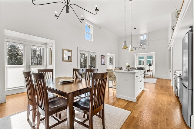 dining space with a towering ceiling, an inviting chandelier, light wood-type flooring, and french doors