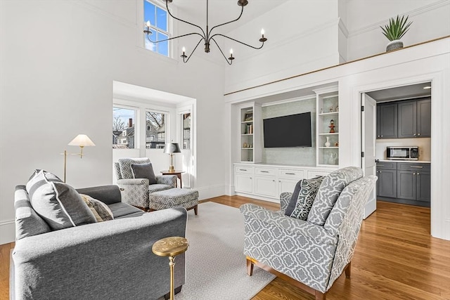 living room featuring built in shelves, wood-type flooring, a chandelier, and a high ceiling