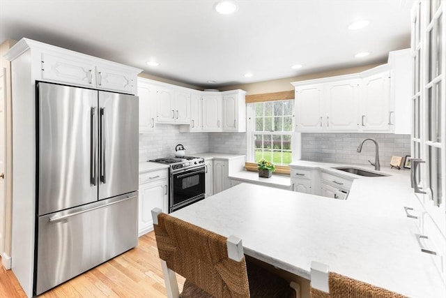 kitchen with a peninsula, a sink, stainless steel fridge, white cabinetry, and gas range oven