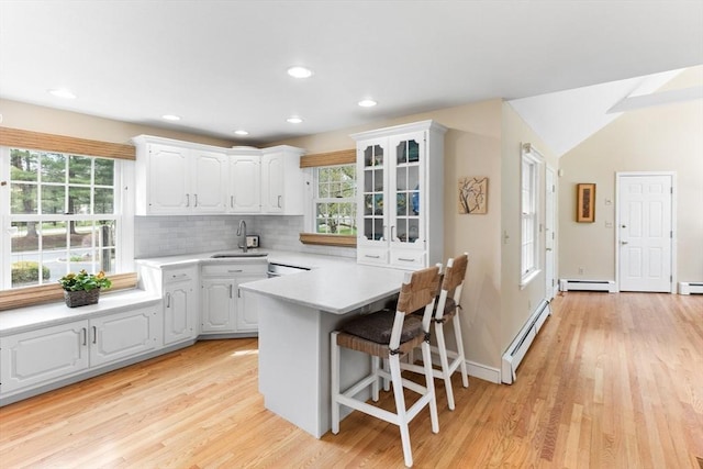 kitchen featuring a baseboard radiator, a sink, light wood-type flooring, light countertops, and white cabinetry