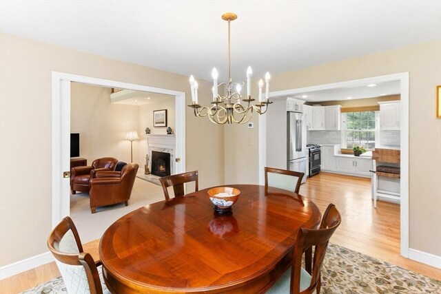 dining space with light wood-type flooring, baseboards, an inviting chandelier, recessed lighting, and a high end fireplace