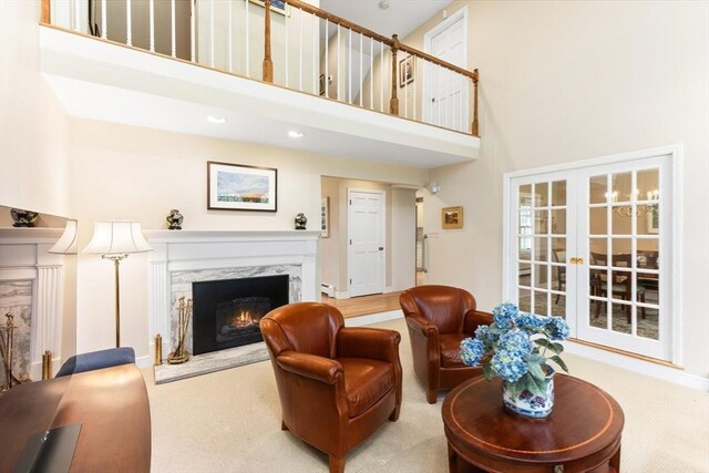 living area featuring french doors, carpet flooring, a towering ceiling, and a premium fireplace
