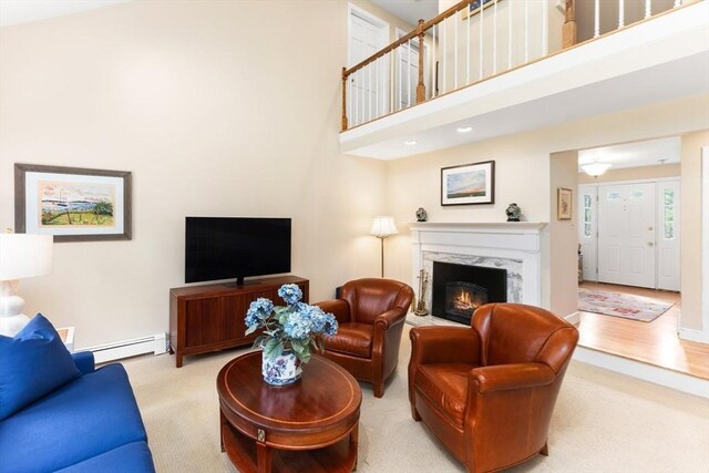 living area featuring baseboard heating, carpet floors, a high ceiling, and a premium fireplace