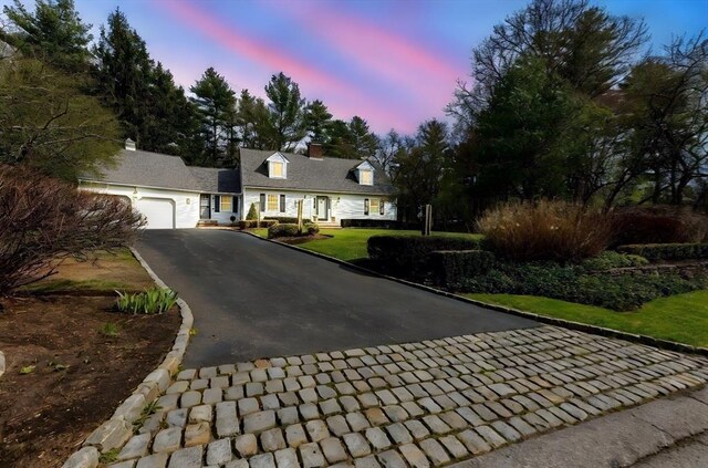 new england style home with a chimney, aphalt driveway, and a garage