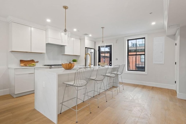 kitchen featuring high end refrigerator, a center island with sink, white cabinetry, light hardwood / wood-style flooring, and hanging light fixtures