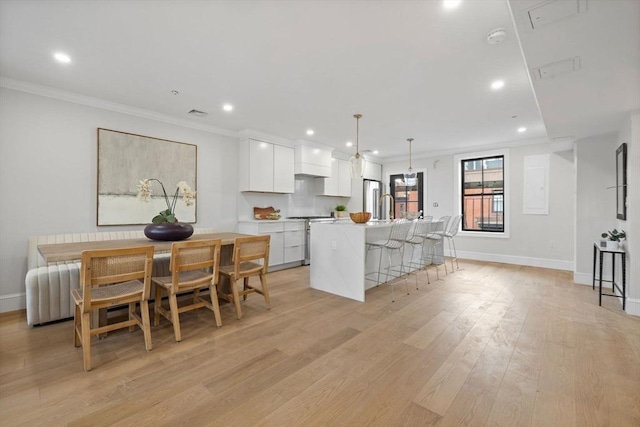 kitchen with ornamental molding, white cabinets, hanging light fixtures, and a kitchen island with sink