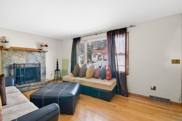 living room with a stone fireplace, wood finished floors, visible vents, and baseboards