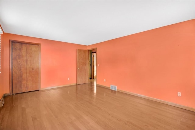 empty room with light wood-style floors, visible vents, and baseboards