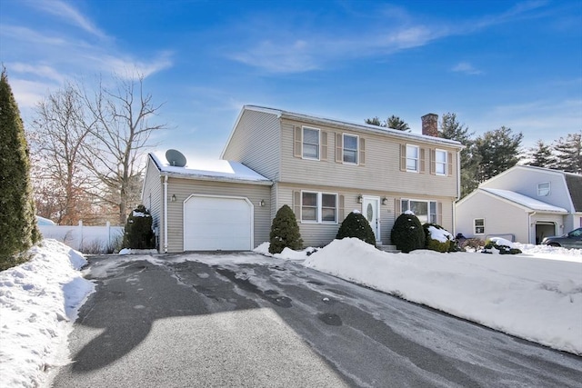 colonial inspired home featuring an attached garage, a chimney, and aphalt driveway