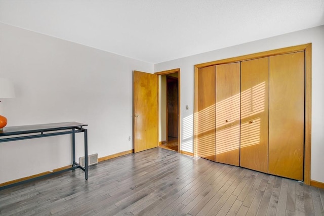 unfurnished bedroom featuring baseboards, a closet, visible vents, and wood finished floors