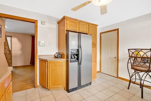 kitchen with stainless steel refrigerator with ice dispenser, light countertops, a ceiling fan, light tile patterned flooring, and baseboards