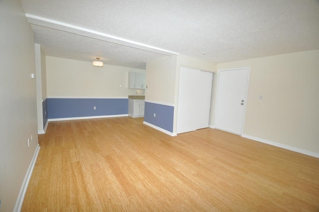 spare room with light wood-style floors, baseboards, and a textured ceiling
