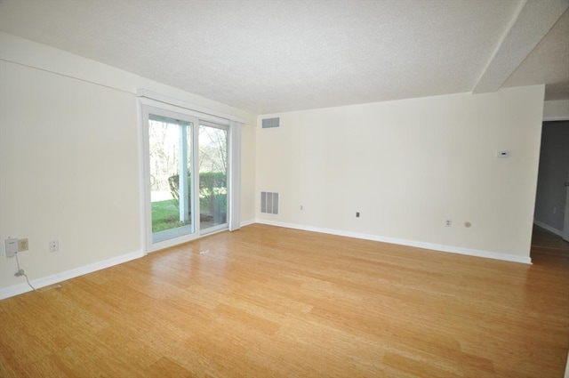 spare room with visible vents, a textured ceiling, light wood finished floors, and baseboards