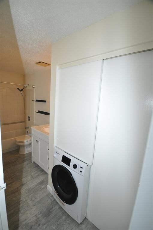 clothes washing area featuring laundry area, light wood finished floors, a textured ceiling, stacked washing maching and dryer, and visible vents