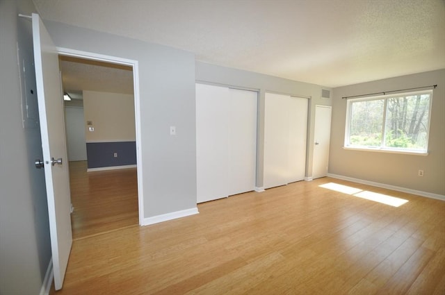 unfurnished bedroom with baseboards, two closets, and light wood-type flooring