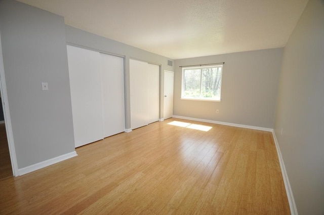 unfurnished bedroom with baseboards, multiple closets, visible vents, and light wood-style floors