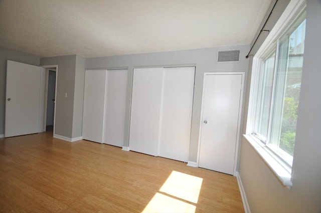 unfurnished bedroom featuring visible vents, multiple closets, light wood finished floors, and baseboards