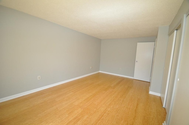 empty room featuring baseboards, light wood finished floors, and a textured ceiling